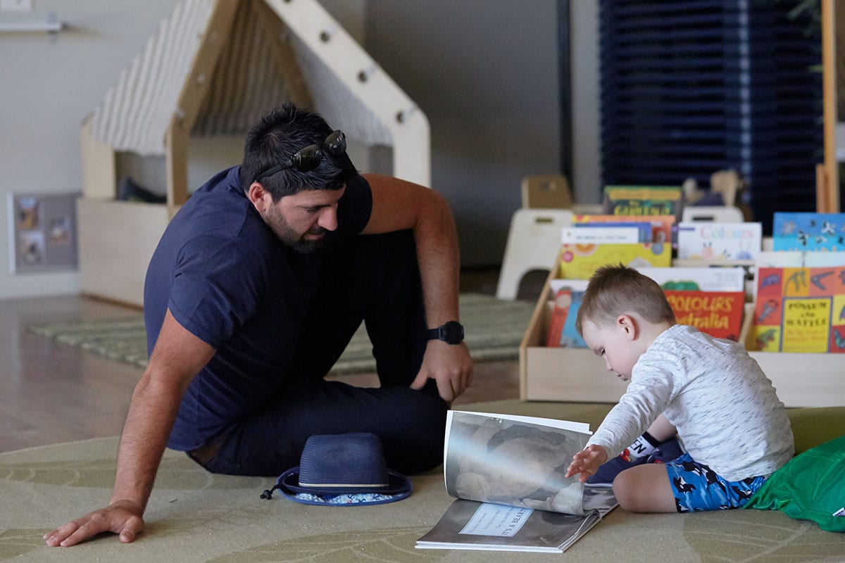 father reading books with young child in daycare setting