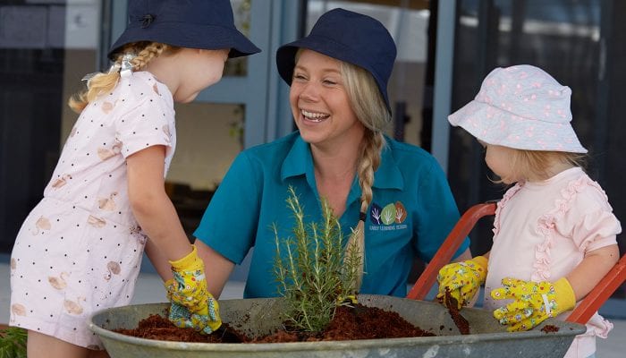 Early Childhood Educator smiling while gardening with two children
