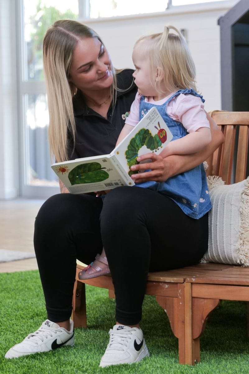 educator reading to child on wooden bench