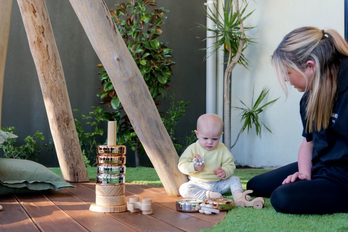 educator with baby outdoors playing with blocks and rings